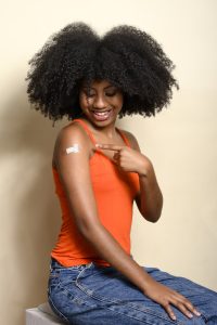 Black teen girl points to the sticker on her arm, smiles and shows that she has been vaccinated
