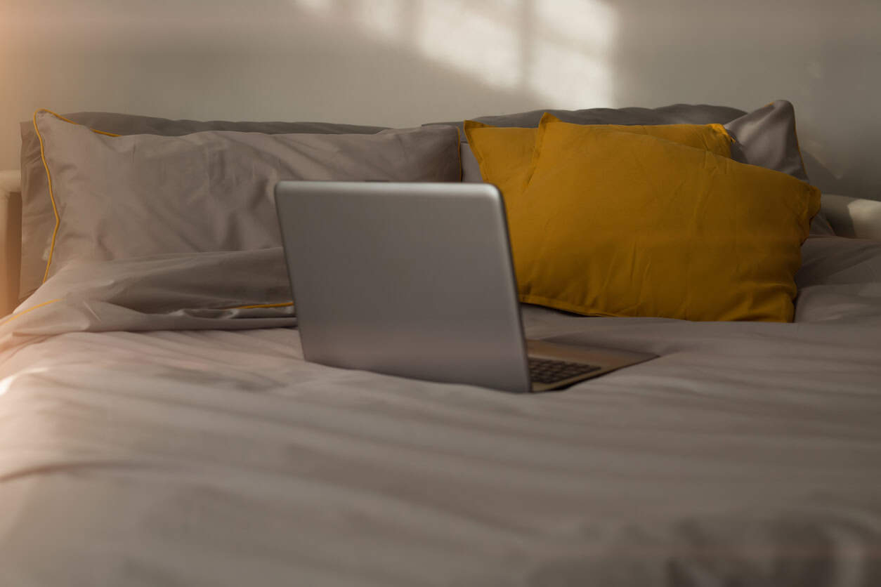 Bedroom, workplace during a pandemic bed with a laptop in the early morning. Trendy colors 2021, interior design