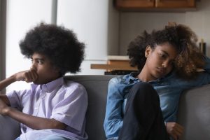 Silent African young couple sit separately on sofa after fight