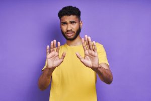 Worried African man gesturing stop sign while standing against purple background